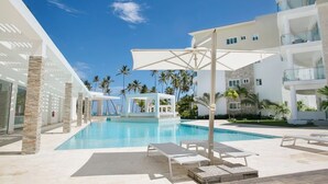 A pool area with lounge chairs, a covered seating area, and a building with balconies. - Luxury 3BR beachfront Condo in Punta Cana (Punta Cana)