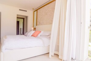 A bedroom with a bed, white curtains, and a door.