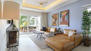 A modern living room with a leather sofa, a dining area with chairs, a table, and a large window. - Luxury 3BR Beachfront Condo in Punta Cana (Punta Cana)