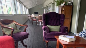 Un área de estar interior acogedora, con un sofá rojo, sillones morados y una mesa de madera con un libro.
