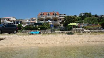 A beachfront property with a sandy beach, a parked car, and a building with multiple balconies and a red roof.