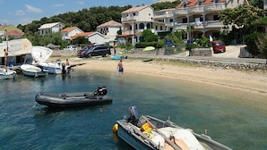 A coastal area with boats docked near a sandy beach, surrounded by multi-story buildings with balconies. - Pansion Gea - Superior Double Room with Balcony and Sea View (Pag)