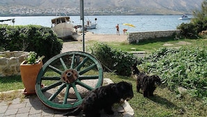 A coastal scene with a large green wheel, a stone wall, and a grassy area with two dogs. - Pansion Gea - Superior Double Room with Balcony and Sea View (Pag)