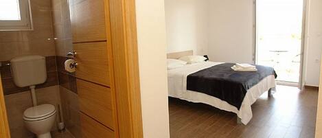 A bedroom with a bed, a bedside table, a hanging light fixture, and a view of the outside.
