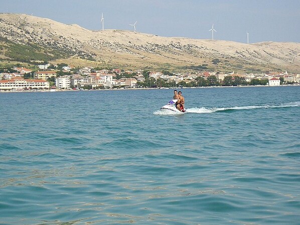 A person jet-skiing on a body of water with buildings and hills in the background.