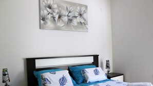 Una cama bien hecha con una colcha azul y blanca de motivos florales, dos almohadas con diseño de concha y una toalla enrollada sobre la cama.