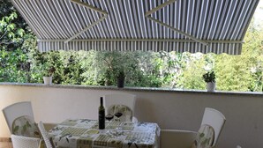 Un patio al aire libre con una mesa dispuesta para dos personas, rodeado de sillas de mimbre, bajo un toldo a rayas.