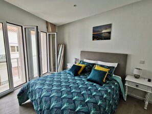 A bedroom with a bed, a nightstand, a painting, and a view through the window.