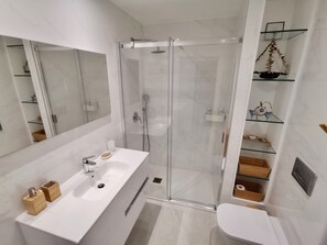 A modern bathroom with a glass-enclosed shower, a white sink with a soap dish, and a toilet.