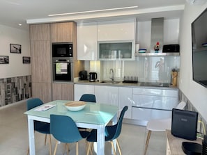 Une cuisine moderne avec une table à manger en verre, des chaises de couleur turquoise et une machine à café.