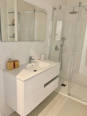 Une salle de bain moderne dotée d’une douche à parois de verre, d’un meuble-lavabo blanc et d’un grand miroir placé au-dessus du meuble-lavabo.