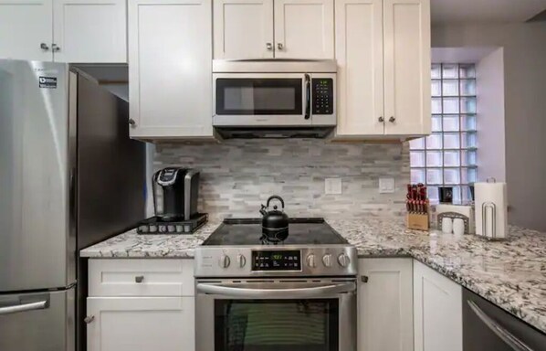 Fully equipped kitchen with stainless steel appliances, white cabinetry, and a tiled backsplash.