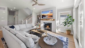 A modern living room with a grey sectional sofa, a wooden coffee table, a fireplace, and a ceiling fan. - Ultimate Beach Getaway (Long Beach)
