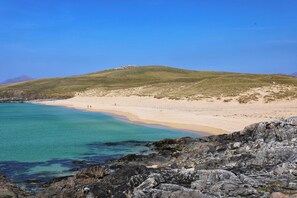Un paisaje costero con una playa arenosa, costa rocosa y una colina cubierta de hierba.
