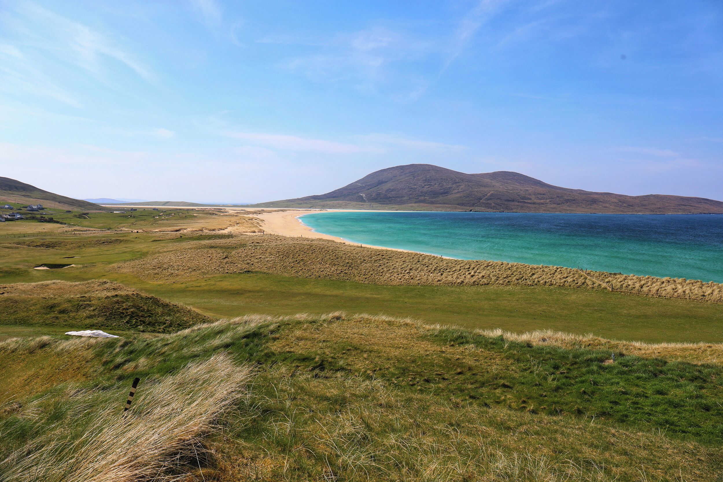 A coastal landscape with a beach, grassy areas, and distant hills.