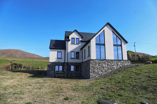 A modern two-story house with a stone foundation, large windows, and a sloped roof. - One Sea (Harris)