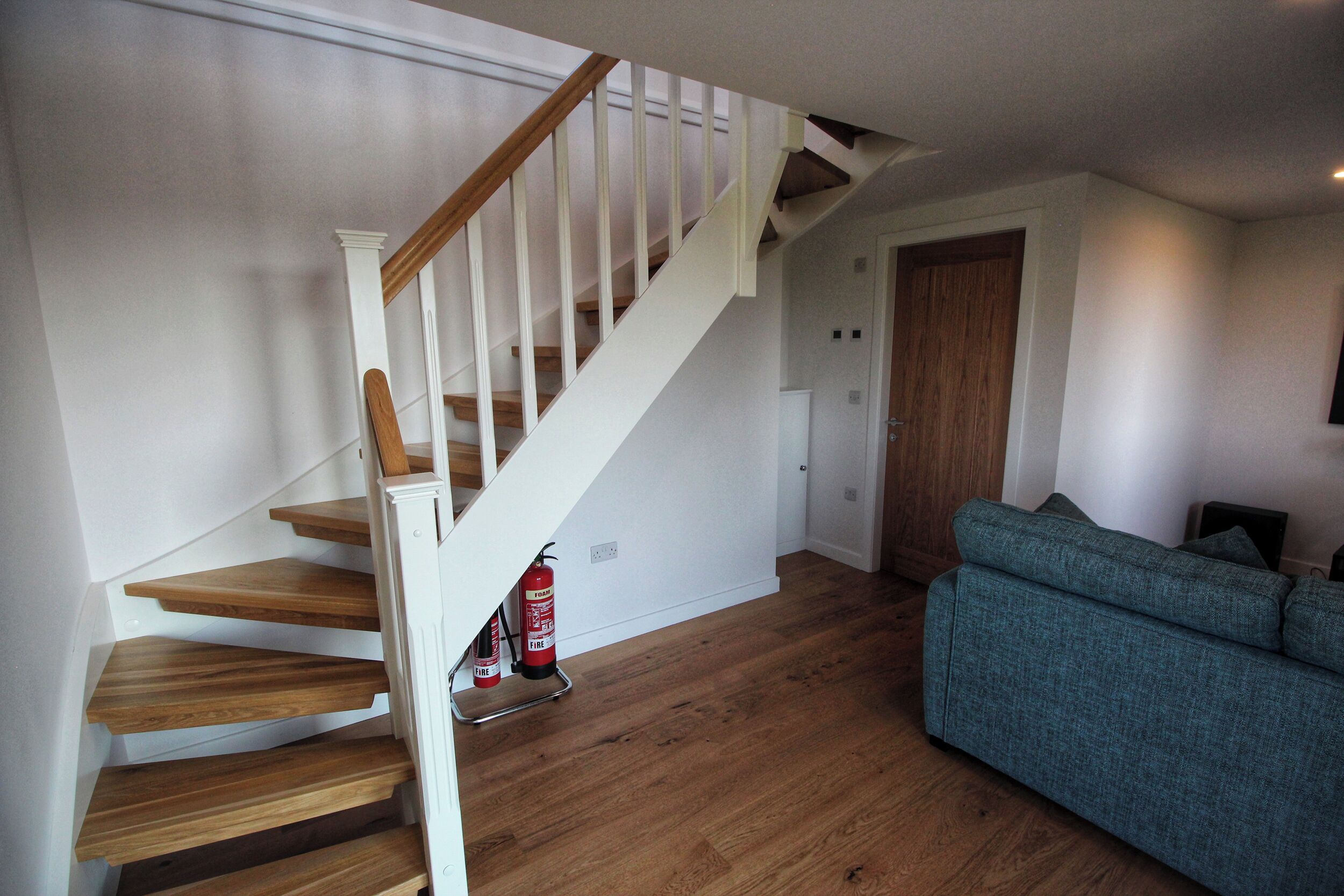 A staircase with wooden steps and white railings, a blue sofa, and a fire extinguisher on the floor.
