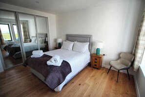 A hotel room with a large bed, two bedside tables, a chair, and a sliding glass door leading to a balcony. - One Sea (Harris)