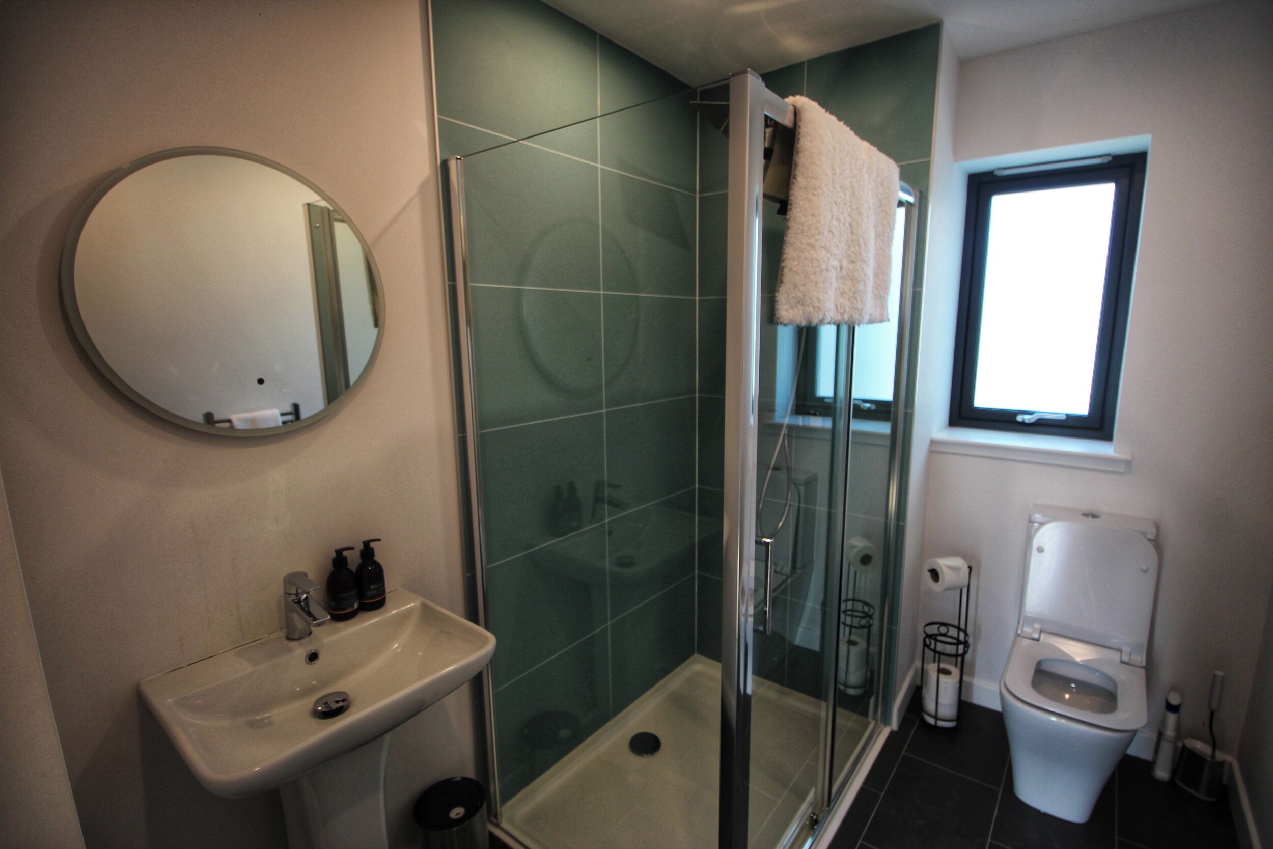 Un baño con ducha de vidrio, lavabo con artículos de aseo y retrete.