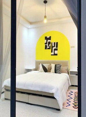 A modern bedroom with a bed, a yellow accent wall, and a unique ceiling design.