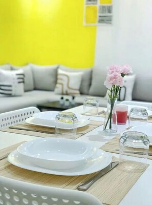 A dining area with a white table set for two, a vase with pink flowers, and a bright yellow wall in the background. - Dreamy Apartment, exceptional view of Majorelle (Marrakech)