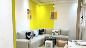 Una sala moderna con sofá, reposapiés, mesa de centro y un comedor con una mesa dispuesta para dos personas.