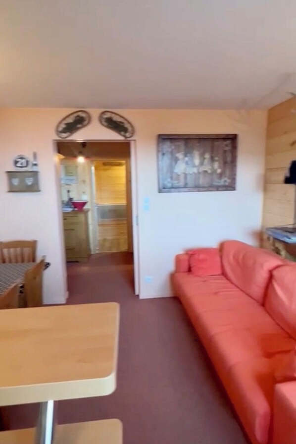 Een kamer met een houten eettafel en stoelen, een rode bank en een keuken in de achtergrond.