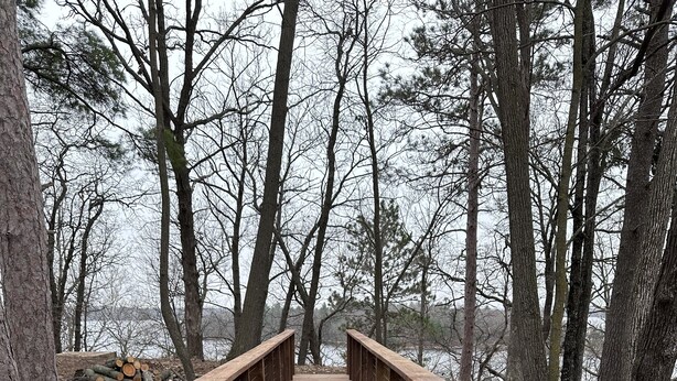 Un pont en bois, doté de garde-corps, qui mène à une zone boisée.