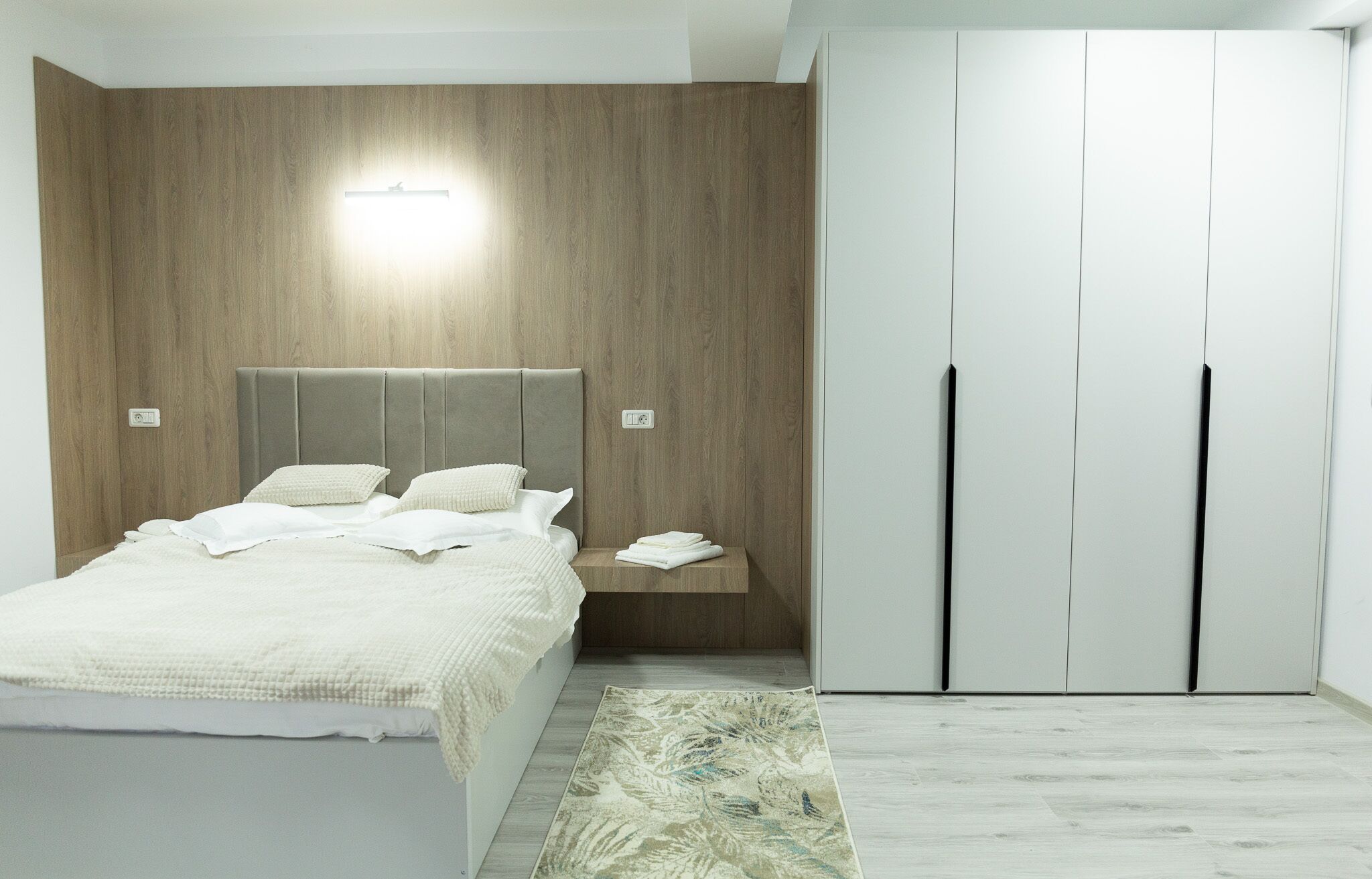 A bedroom with a bed, bedside tables, a wardrobe, and a wall-mounted light.