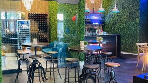 Zona de bar moderna amb parets verdes, detalls de fusta i diferents opcions d'asseients, incloent tamborets i taules.