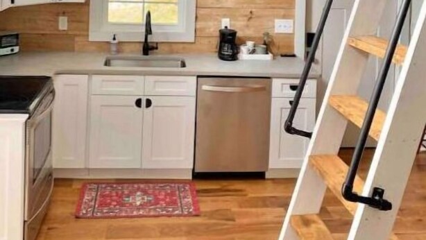 Une cuisine avec des meubles blancs, un plan de travail en bois, une fenêtre et un escalier en bois.