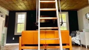 Une pièce de style « loft », avec un plancher en bois, un banc blanc et une échelle menant à un balcon.