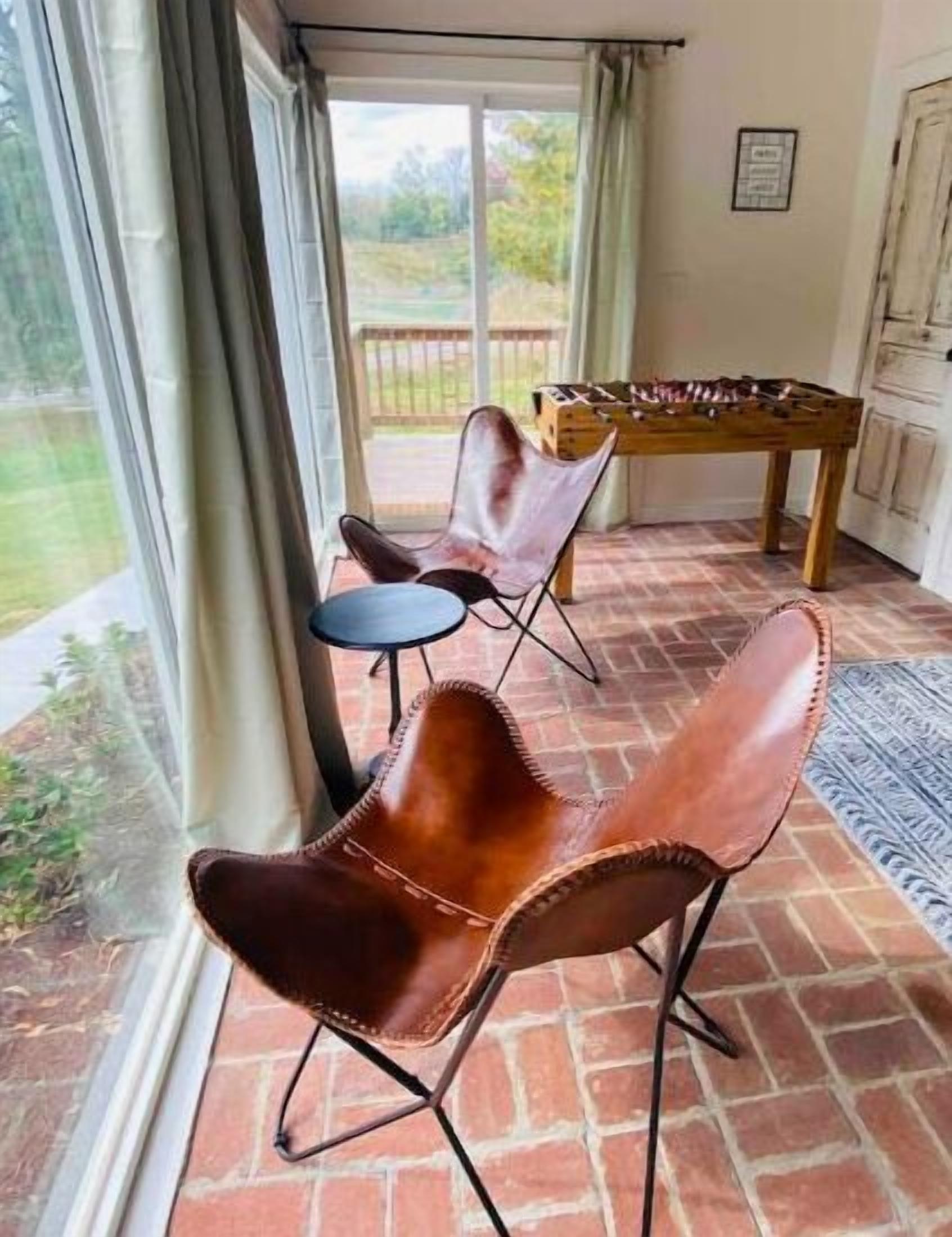 A room with a brick floor, a foosball table, and two leather chairs.