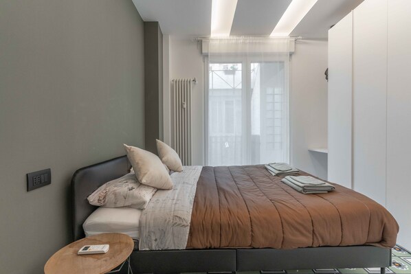 Une chambre à coucher moderne avec un lit, une table de chevet et une fenêtre avec des rideaux.