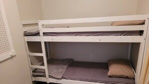 Een stapelbed met twee niveaus, een klein plankje en een raam met gordijn.