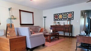 A living room with a sofa, coffee table, wooden dresser, and a desk with a computer. - Rustic Pines Waterfront Cottage *CLEAR WATER* (Kawartha Lakes)