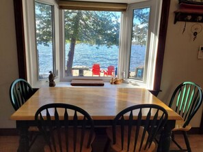 A dining table with four chairs, a view of a lake, and a red chair outside.