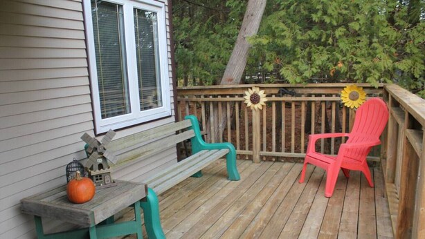 A wooden deck with a bench and a chair, a small table with a pumpkin decoration, and a sunflower decoration on the railing. - Rustic Pines Waterfront Cottage *CLEAR WATER* (Kawartha Lakes)
