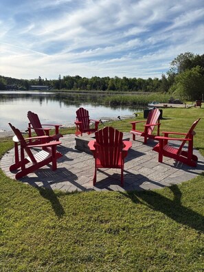 A lakeside setting with red Adirondack chairs arranged around a circular stone patio.