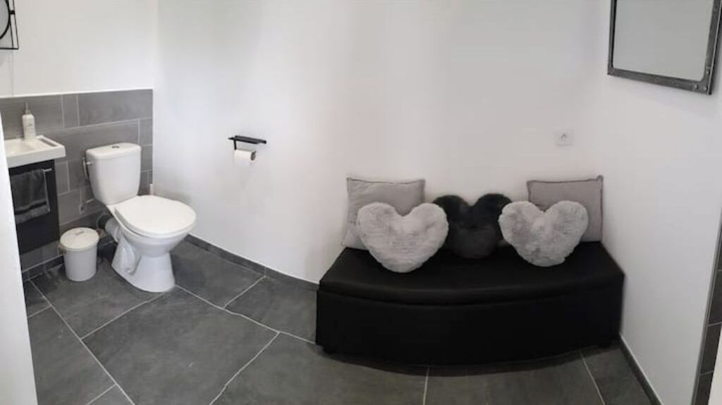 A bathroom with a toilet, sink, and two heart-shaped cushions on a bench.