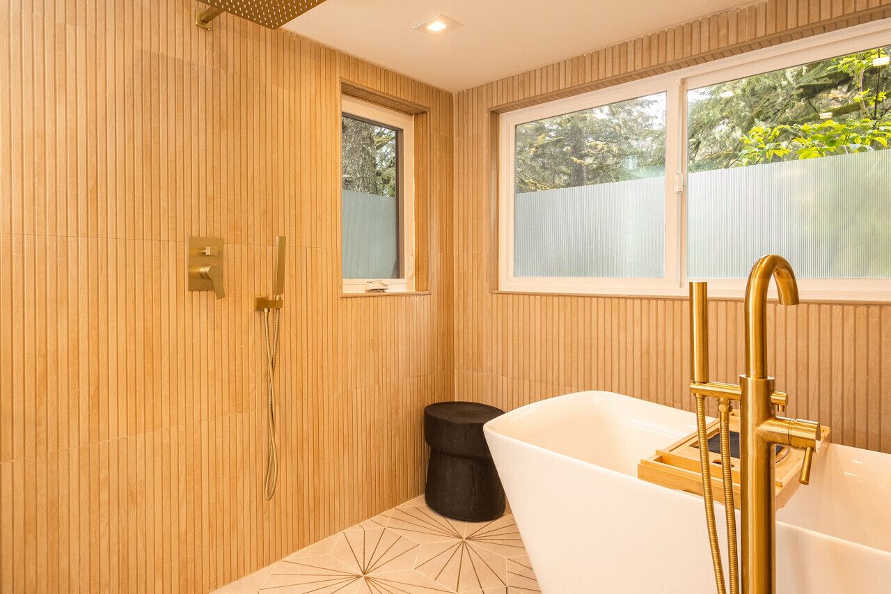 A modern bathroom with a freestanding bathtub, a shower, and a window providing a view of greenery outside.