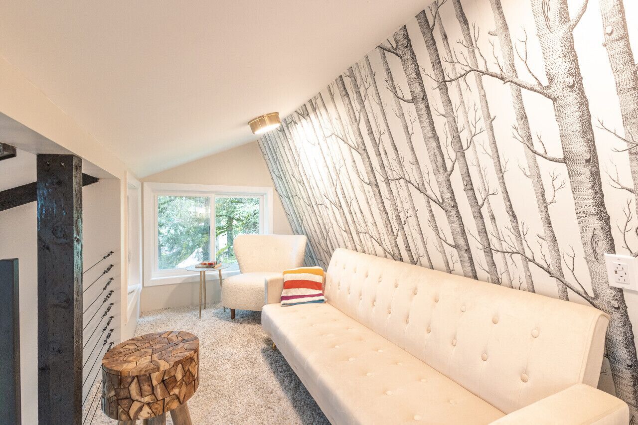 A modern living room with a white sofa, a wooden stool, and a wall with a tree pattern.