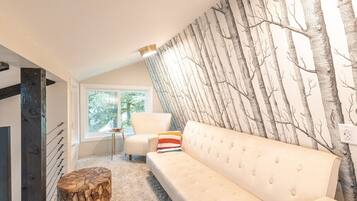 A modern living room with a white sofa, a wooden stool, and a wall with a tree pattern.