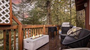 A wooden deck with a fire pit, outdoor grill, and wicker chairs.