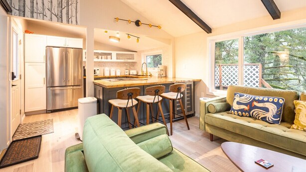 A modern kitchen with a stainless steel refrigerator, wooden chairs, and a bar area.