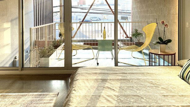 Ein modernes Schlafzimmer mit einem großen Bett, einem Balkon mit einem gelben Sessel und Blick auf die Stadt.