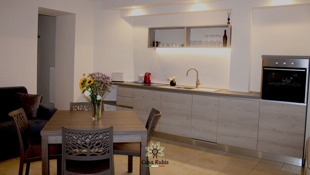 A modern kitchen with a dining area, featuring a wooden dining table, chairs, a vase with flowers, a built-in oven, and a wine rack. - CASA DEGLI AMICI (Ruvo di Puglia)