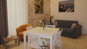 A dining area with a white table and chairs, a grey sofa, and a stone wall with artwork. - CASA DEGLI AMICI (Ruvo di Puglia)