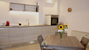 A modern kitchen with a wooden dining table, a vase of flowers, and a built-in oven. - CASA DEGLI AMICI (Ruvo di Puglia)
