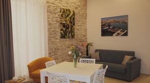 A dining area with a white table and chairs, a grey sofa, and a stone wall with artwork.